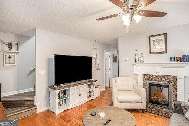 living room featuring ceiling fan, a premium fireplace, light hardwood / wood-style flooring, and a textured ceiling