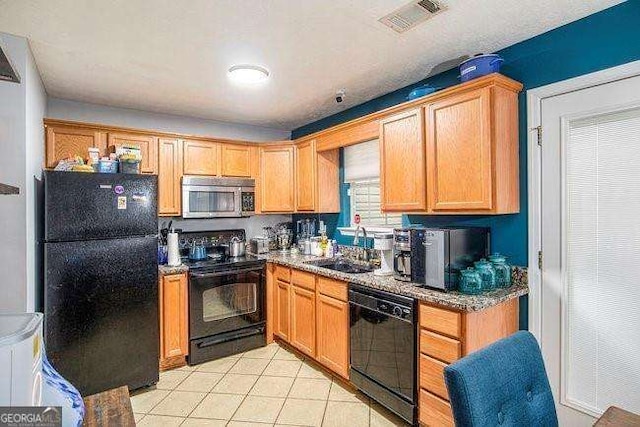 kitchen with sink, light tile patterned flooring, black appliances, and stone countertops