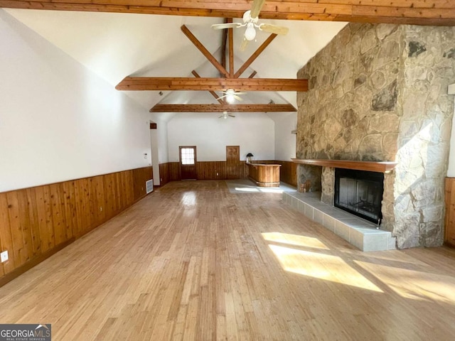 unfurnished living room featuring beam ceiling, light hardwood / wood-style flooring, a tile fireplace, and wooden walls