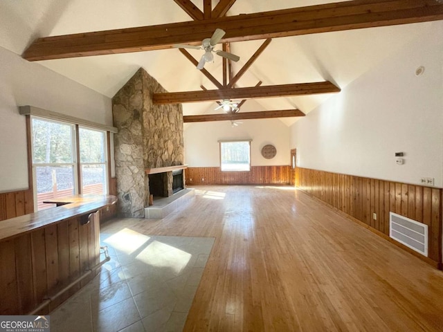 unfurnished living room featuring beamed ceiling, a fireplace, wooden walls, and light hardwood / wood-style floors