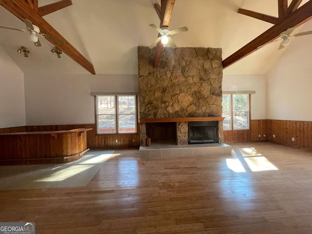 unfurnished living room featuring beam ceiling, a fireplace, ceiling fan, and wood walls