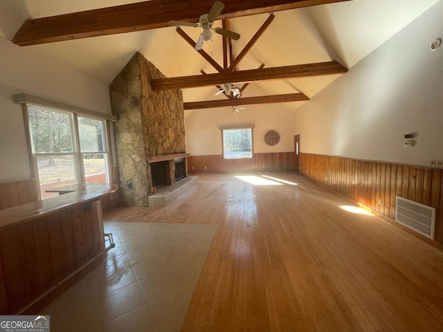 unfurnished living room featuring wooden walls, a fireplace, beamed ceiling, wood-type flooring, and ceiling fan