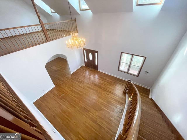 interior space featuring a towering ceiling, a chandelier, hardwood / wood-style floors, and a skylight