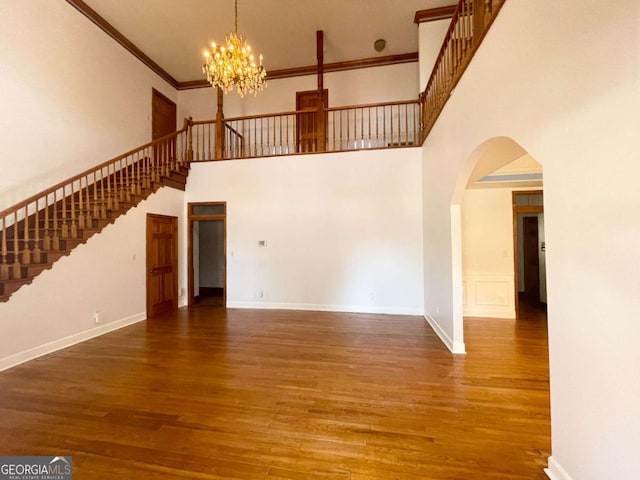 unfurnished living room with crown molding, dark hardwood / wood-style floors, a chandelier, and a high ceiling