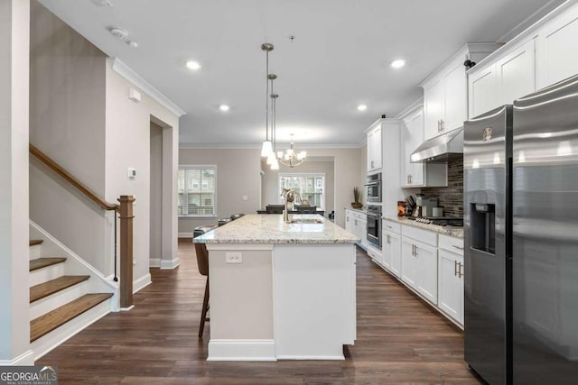 kitchen with pendant lighting, sink, white cabinets, stainless steel appliances, and a center island with sink