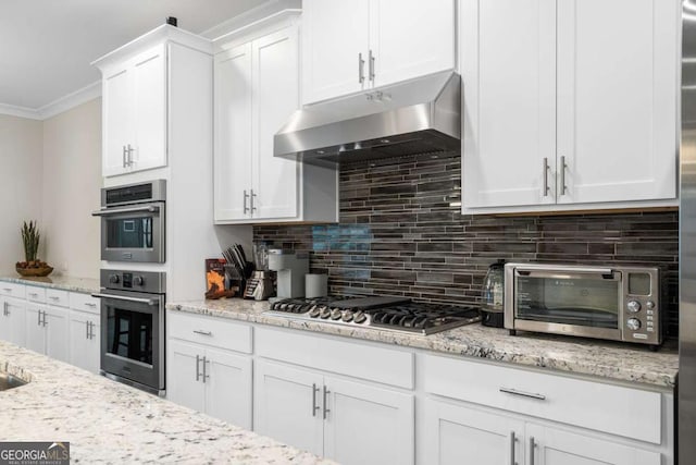 kitchen with appliances with stainless steel finishes, tasteful backsplash, white cabinetry, ornamental molding, and light stone counters