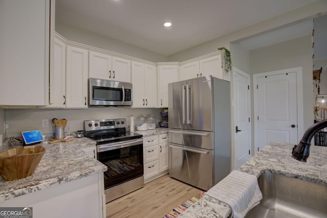 kitchen featuring appliances with stainless steel finishes, white cabinetry, sink, light stone counters, and light hardwood / wood-style floors