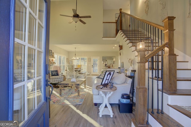 living room with ceiling fan with notable chandelier, hardwood / wood-style floors, and a high ceiling