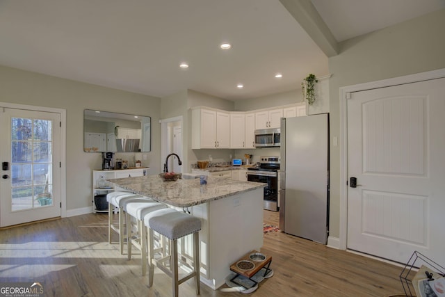 kitchen featuring white cabinetry, an island with sink, a breakfast bar area, light stone counters, and stainless steel appliances