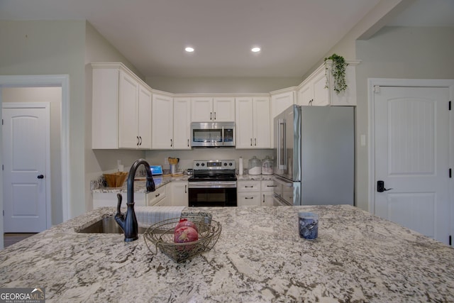 kitchen featuring stainless steel appliances, light stone countertops, sink, and white cabinets