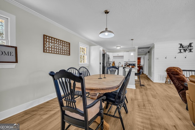 dining space featuring ornamental molding, sink, light hardwood / wood-style flooring, and a textured ceiling