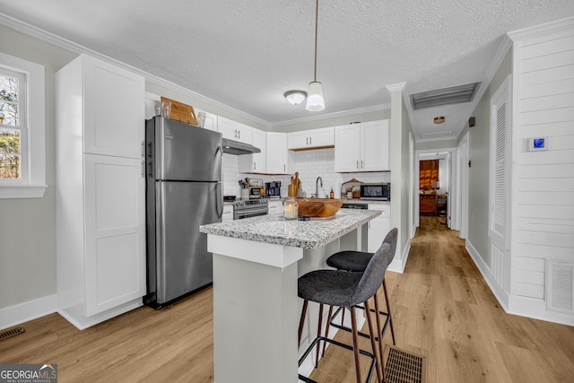 kitchen featuring a kitchen island, appliances with stainless steel finishes, decorative light fixtures, white cabinetry, and a kitchen bar