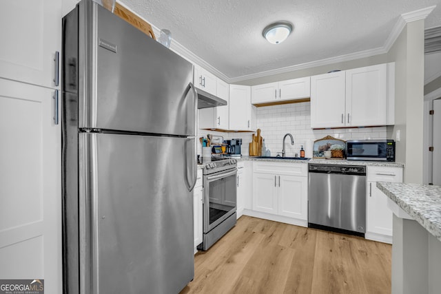 kitchen with appliances with stainless steel finishes, sink, white cabinets, ornamental molding, and light stone countertops