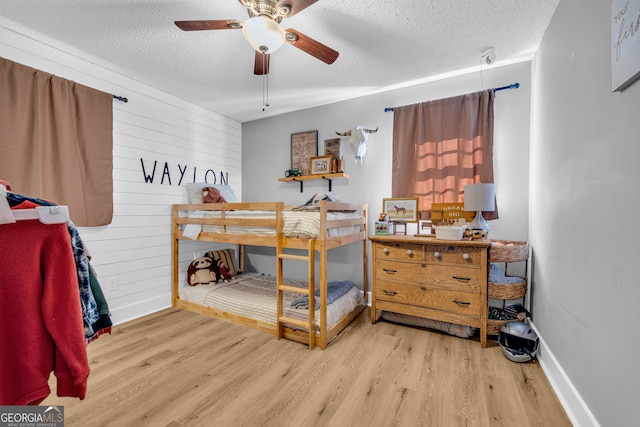 bedroom featuring ceiling fan, wooden walls, light hardwood / wood-style floors, and a textured ceiling