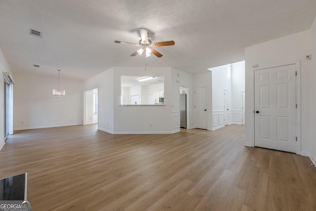 unfurnished living room featuring ceiling fan with notable chandelier, a textured ceiling, and light wood-type flooring