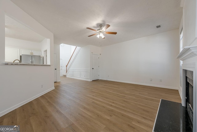 unfurnished living room with a textured ceiling, ceiling fan, and light wood-type flooring