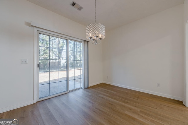 spare room with an inviting chandelier and hardwood / wood-style floors