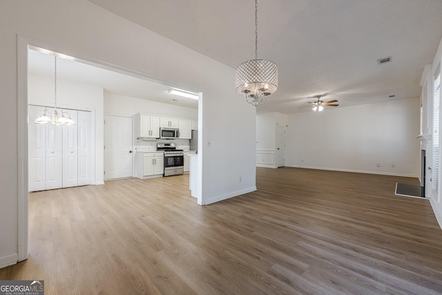 unfurnished living room featuring ceiling fan with notable chandelier and light hardwood / wood-style floors