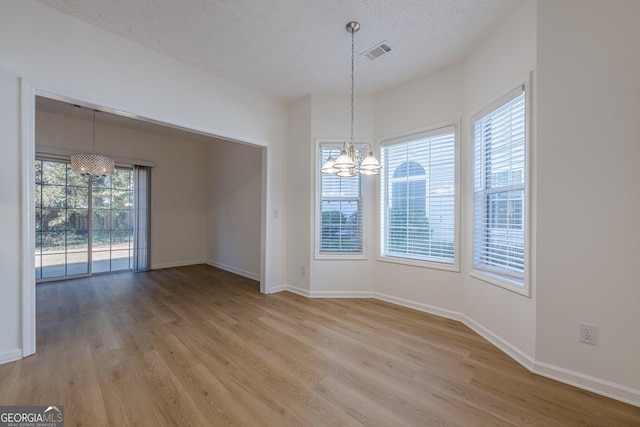 unfurnished dining area featuring an inviting chandelier, light hardwood / wood-style flooring, and a textured ceiling