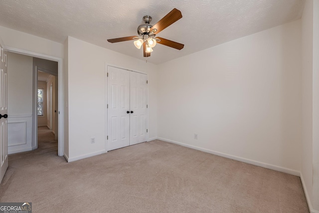 unfurnished bedroom featuring ceiling fan, a closet, light carpet, and a textured ceiling