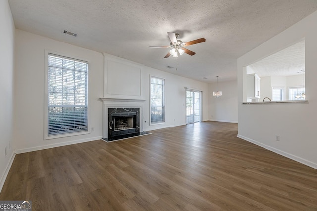 unfurnished living room featuring dark wood-type flooring, ceiling fan with notable chandelier, a textured ceiling, and a high end fireplace