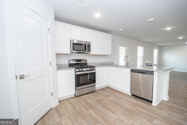 kitchen with appliances with stainless steel finishes, sink, white cabinets, and light wood-type flooring