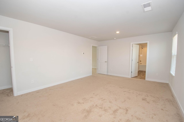 unfurnished bedroom with light colored carpet, a spacious closet, ensuite bath, and a closet