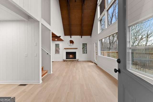 unfurnished living room featuring light wood finished floors, visible vents, stairway, a brick fireplace, and high vaulted ceiling