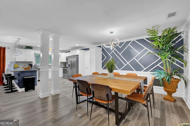 dining area with decorative columns, ornamental molding, and light wood-type flooring