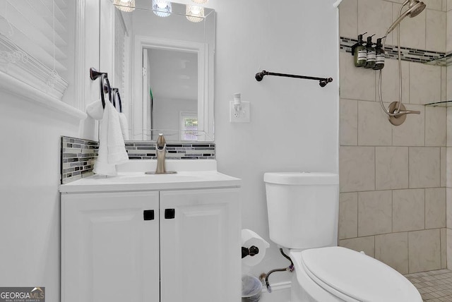 bathroom with vanity, toilet, a tile shower, and backsplash