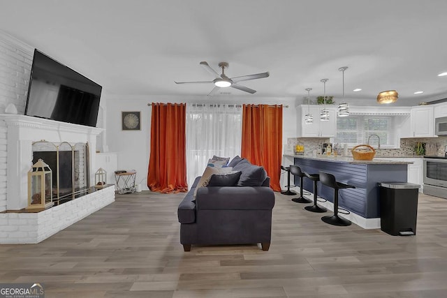 living room featuring crown molding, ceiling fan, a fireplace, and light wood-type flooring