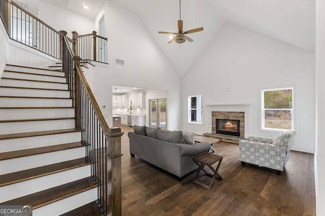 living room with a stone fireplace, dark wood-type flooring, a wealth of natural light, and high vaulted ceiling