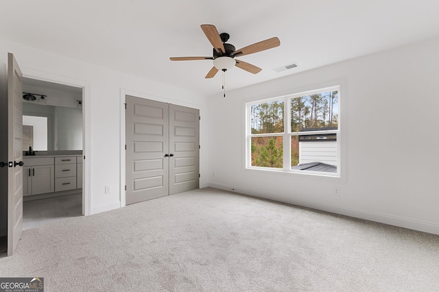 unfurnished bedroom with ensuite bathroom, light carpet, ceiling fan, and a closet