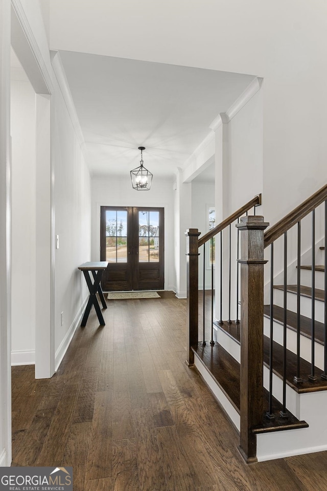 foyer entrance with dark hardwood / wood-style flooring, a notable chandelier, crown molding, and french doors