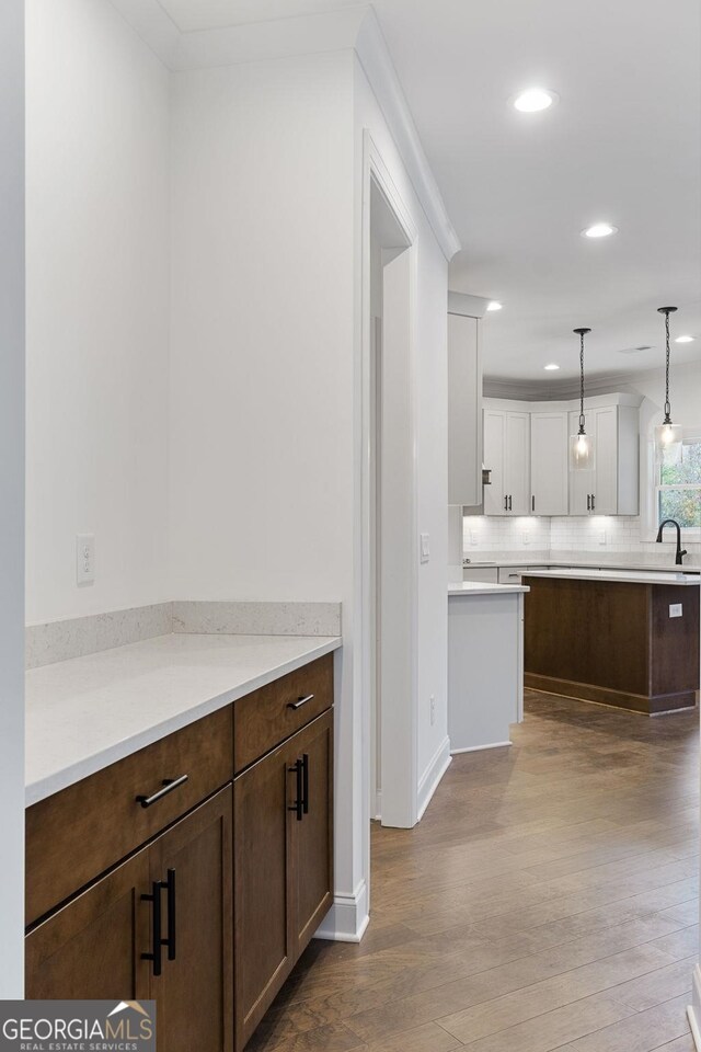 kitchen featuring sink, decorative light fixtures, light wood-type flooring, white cabinets, and backsplash