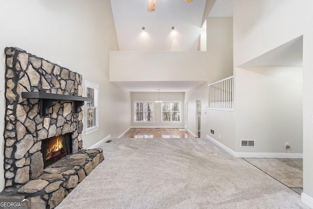 unfurnished living room with a stone fireplace, a high ceiling, and carpet flooring