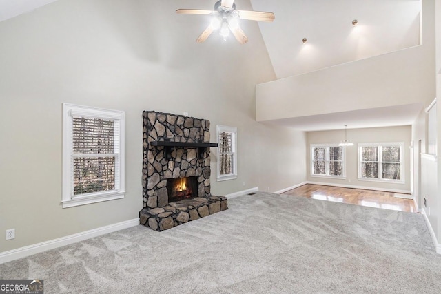 carpeted living room with a stone fireplace, ceiling fan with notable chandelier, and high vaulted ceiling