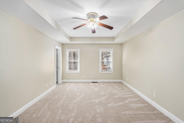 carpeted spare room with ceiling fan and a raised ceiling