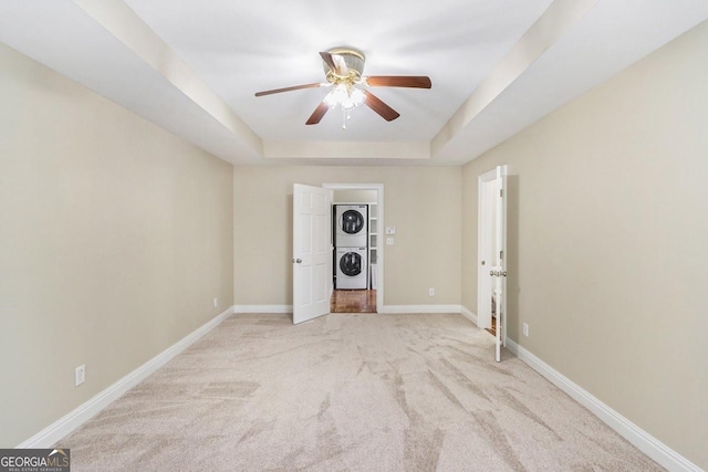 empty room featuring ceiling fan, stacked washer / dryer, a raised ceiling, and light carpet