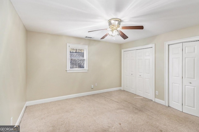 unfurnished bedroom featuring multiple closets, light colored carpet, and ceiling fan