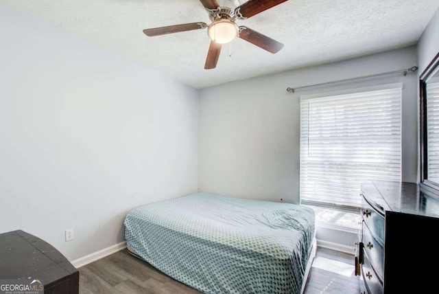 bedroom with multiple windows, ceiling fan, dark wood-type flooring, and a textured ceiling