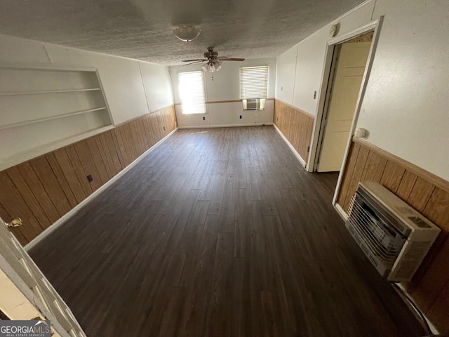 unfurnished living room featuring dark wood-type flooring, wood walls, a textured ceiling, built in features, and ceiling fan