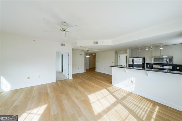 kitchen with a kitchen bar, gray cabinetry, light hardwood / wood-style flooring, appliances with stainless steel finishes, and ceiling fan