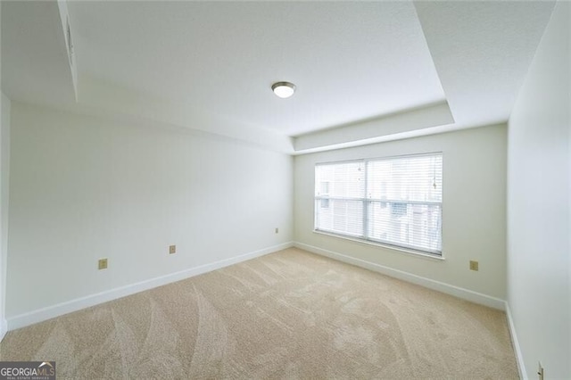 empty room with a raised ceiling and light carpet