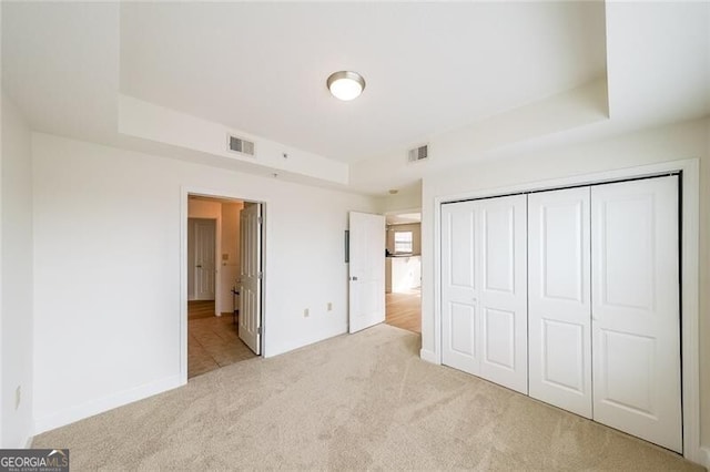 unfurnished bedroom featuring a tray ceiling, light colored carpet, a closet, and ensuite bathroom