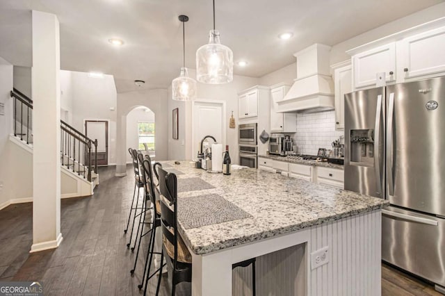 kitchen with a large island, appliances with stainless steel finishes, a kitchen breakfast bar, decorative light fixtures, and custom exhaust hood