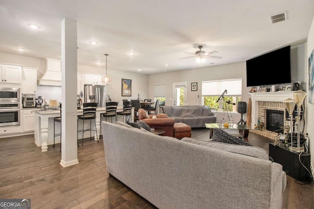 living room with ceiling fan, a fireplace, and dark hardwood / wood-style flooring