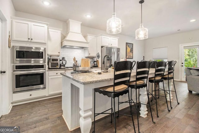 kitchen featuring stainless steel appliances, custom exhaust hood, a kitchen island with sink, and white cabinetry