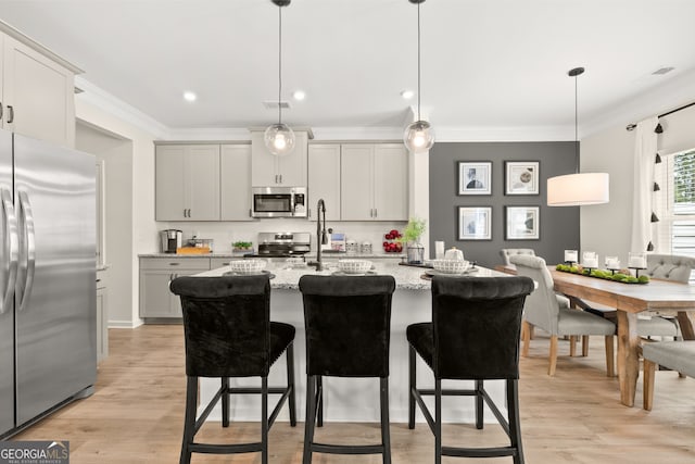 kitchen featuring pendant lighting, stainless steel appliances, light stone counters, and a center island with sink