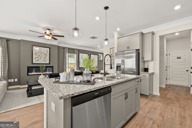 kitchen featuring gray cabinetry, light stone counters, a center island with sink, pendant lighting, and stainless steel appliances